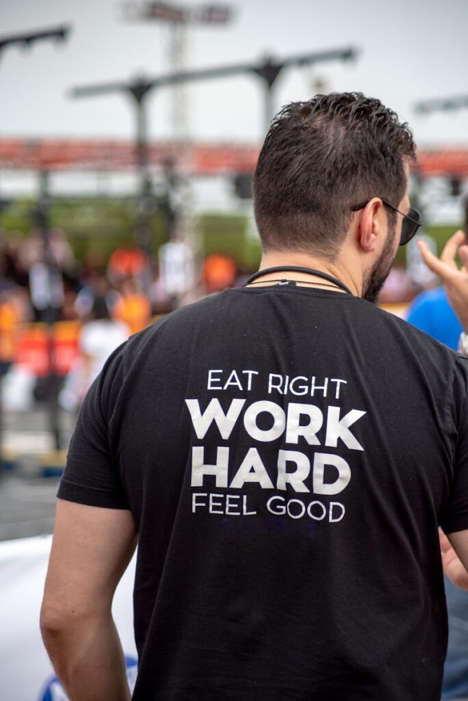 Back view of a man wearing a motivational t-shirt at an outdoor gathering.